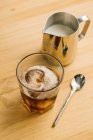 De cima de vidro elegante com gelo café preto na mesa de madeira com jarro de leite e colher — Fotografia de Stock