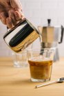 Professionelle gesichtslose Barista gießt Milch aus Metallkanne in Glas mit frischem Eiskaffee auf Holztisch im Café — Stockfoto