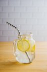 Металлическая многоразовая солома и стеклянный кувшин со льдом и ломтиками лимона на деревянном столе на кухне — стоковое фото