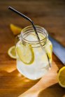 De cima palha reutilizável metálica e jarro de vidro com gelo e limão fatias na mesa de madeira na cozinha — Fotografia de Stock