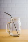 Several shiny steel straws in empty glass jug with handle on wooden table — Stock Photo