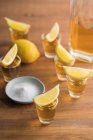 De arriba tiros de vidrio de tequila dorado con borde salado y rodajas de limón en la parte superior de la mesa de madera - foto de stock