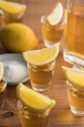 De arriba tiros de vidrio de tequila dorado con borde salado y rodajas de limón en la parte superior de la mesa de madera - foto de stock