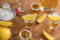 Da sopra vista dall'alto di colpi di vetro di tequila dorata con bordo salato e fette di limone in cima sul tavolo di legno — Foto stock