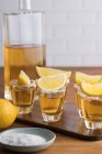 Von oben Glasaufnahmen von goldenem Tequila mit salzigem Rand und Zitronenscheiben auf dem Holztisch — Stockfoto