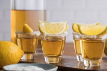 Dall'alto bicchierini di tequila dorata con bordo salato e fette di limone in cima sul tavolo di legno — Foto stock