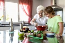 Alegre anciana con cabello blanco ayudando a su hijo mientras preparan guacamole juntos en la cocina - foto de stock