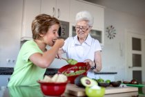 Cheerful grandma and boy tasting homemade guacamole paste with tortilla chips in kitchen — Stock Photo