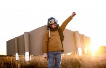 Щаслива дитина в окулярах і картонних крилах піднімає руки під час гри на полі під підсвічуванням — стокове фото