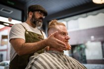 Barbiere fare massaggio viso a bello rossa uomo con seduta in sedia — Foto stock