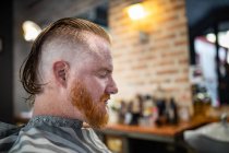 Side view of redhead man sitting in modern barbershop with closed eyes waiting for barber — Stock Photo