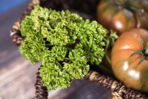 Primo piano dall'alto di verde fresco e pomodori rossi in cesto sul tavolo — Foto stock