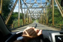 Unrecognizable person steering vehicle on asphalt road towards modern bridge on sunny day in Costa Rica — Stock Photo