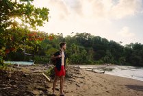 Jóvenes viajeros masculinos enfocados disfrutando del paisaje marino mientras están de pie en la costa arenosa de Costa Rica - foto de stock
