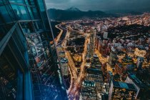 From above magnificent view night city from viewpoint in contemporary high rise building with glass walls in downtown against mountain with snowy peak at horizon at night — Stock Photo