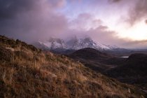 Paisagem pitoresca de planalto selvagem com montanhas nevadas picos e cumes entre nuvens dramáticas durante o pôr do sol — Fotografia de Stock