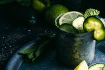 De dessus tasse en métal de boisson de désintoxication au concombre froid avec des tranches de citron vert et des feuilles de menthe placées sur le plateau — Photo de stock