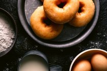 Top view of fresh doughnuts placed on rough table near various pastry ingredients and utensils in kitchen — Stock Photo