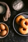 Top view of fresh doughnuts placed on rough table near various pastry ingredients and utensils in kitchen — Stock Photo