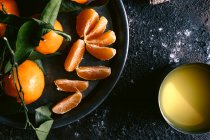 Vista dall'alto della tazza con succo di frutta fresco e piatto con mandarini maturi disposti su tavolo nero grezzo vicino al tovagliolo — Foto stock