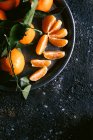 Вид сверху кружки со свежим фруктовым соком и тарелки со спелыми танжеринами, расположенные на черном столе рядом с салфеткой — стоковое фото