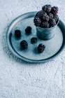 From above cup with ripe blackberries placed on metal tray on plaster surface — Stock Photo