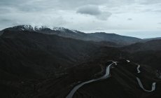 From above of empty asphalt winding road on black powerful mountains with cloudy grey sky on background — Stock Photo