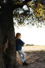 Entzückend ernstes kleines Mädchen in Freizeitkleidung, das an einem sonnigen Sommertag in der Natur neben einem Baum steht und Ukulele spielt — Stockfoto