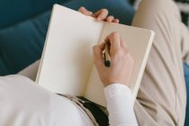 From above faceless woman in white shirt sitting on sofa and writing in notebook working on business project — Stock Photo