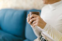 Cortada mulher irreconhecível segurando caneca de café sentado no sofá acolhedor no escritório — Fotografia de Stock