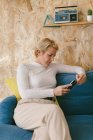 Donna d'affari adulta con acconciatura corta seduta nel tempo libero sul divano e navigando sul cellulare in ufficio — Foto stock