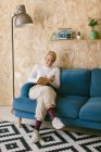 Весела блондинка з коротким волоссям у білій сорочці сидить на дивані і пише в блокноті, працюючи над бізнес-проектом — стокове фото