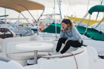 Vista laterale della giovane donna in maglione casual sorridente mentre naviga sul cellulare in yacht moderno — Foto stock