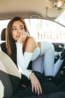 Annoiato giovane donna sensibile affascinante in abiti casual guardando altrove mentre in piedi sulle ginocchia e appoggiato sul sedile in auto — Foto stock