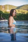 Снизу чувственная молодая очаровательная женщина в купальнике, смотрящая в камеру, стоя в глубине озера в сельской местности — стоковое фото