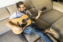 Stilvoller Gitarrist auf Couch im Wohnzimmer — Stockfoto