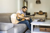 Homem alegre com guitarra verificando smartphone no sofá — Fotografia de Stock