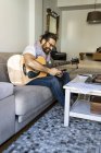 Веселый мужчина с проверяющим гитару смартфоном на диване — стоковое фото