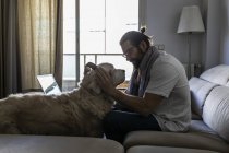 Случайный парень, надевающий наушники на собаку в гостиной — стоковое фото