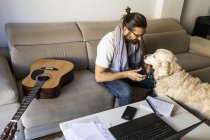 Casual guy putting headphones on dog in living room — Stock Photo