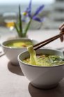 De cima cortado pessoa irreconhecível segurando uma tigela de ramen oriental sopa de macarrão saudável com shiitake, espinafre, cenouras, ovos e pimentas na mesa do restaurante — Fotografia de Stock