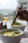 D'en haut cultivé personne méconnaissable tenant un bol de ramen oriental soupe de nouilles saines avec shiitake, épinards, carottes, oeufs et piments sur la table du restaurant — Photo de stock