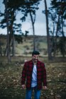 Cheerful man in casual wear standing among evergreen coniferous trees in autumn countryside — Stock Photo