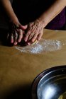 Неузнаваемая леди катит маленькие шарики из мягкого теста во время приготовления теста на столе на кухне — стоковое фото