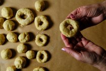 Vue du dessus de la femme anonyme faisant des anneaux de pâte molle tout en préparant des beignets sur la table dans la cuisine — Photo de stock