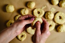 Vue du dessus de la femme anonyme faisant des anneaux de pâte molle tout en préparant des beignets sur la table dans la cuisine — Photo de stock