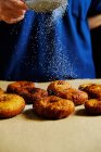 Нерозпізнана людина, яка використовує сито, щоб розлити цукрову пудру на стек свіжих пончиків під час приготування тіста на кухні — стокове фото