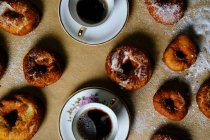 Верхний вид вкусных пончиков с сахарной пудрой и чашки горячего чая помещены на стол дома — стоковое фото