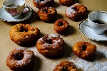 Vista superior de deliciosas rosquillas con azúcar en polvo y tazas de té caliente puestas en la mesa en casa - foto de stock