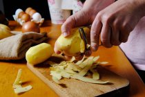 Crop cocinero anónimo pelando patata sobre tabla de cortar de madera en la cocina moderna - foto de stock